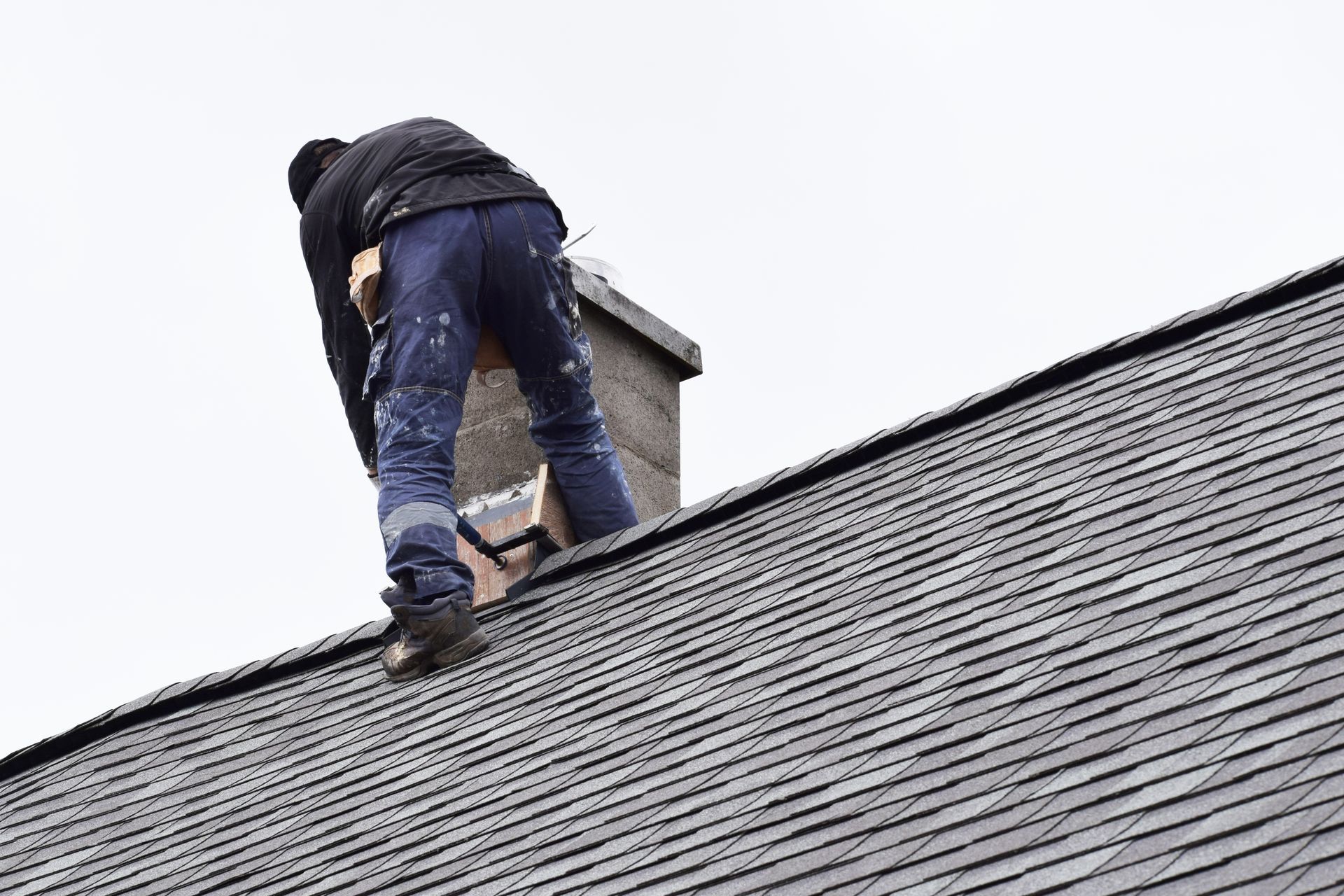 Person climbing onto a rooftop near a chimney under an overcast sky