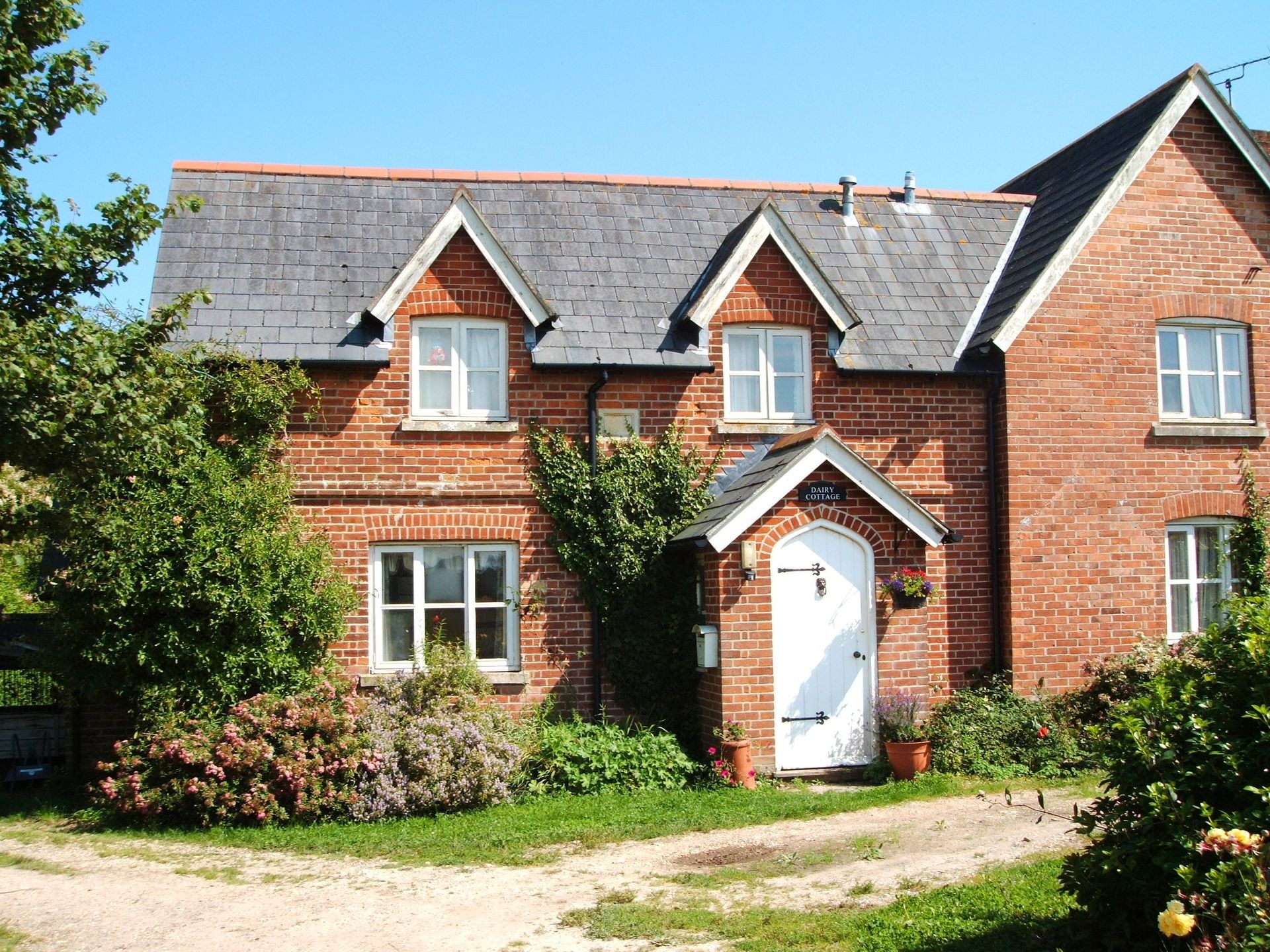 Red-brick house with white front door, dormer windows, and a small garden under a slate roof.