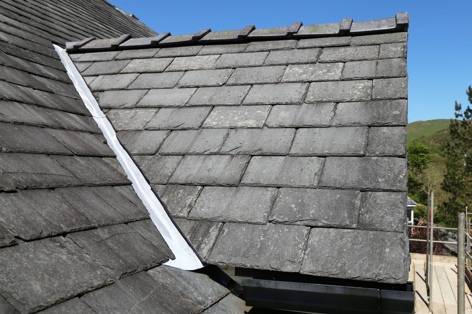 Roof with damaged gray shingles and a white flashing strip between two sloped sections
