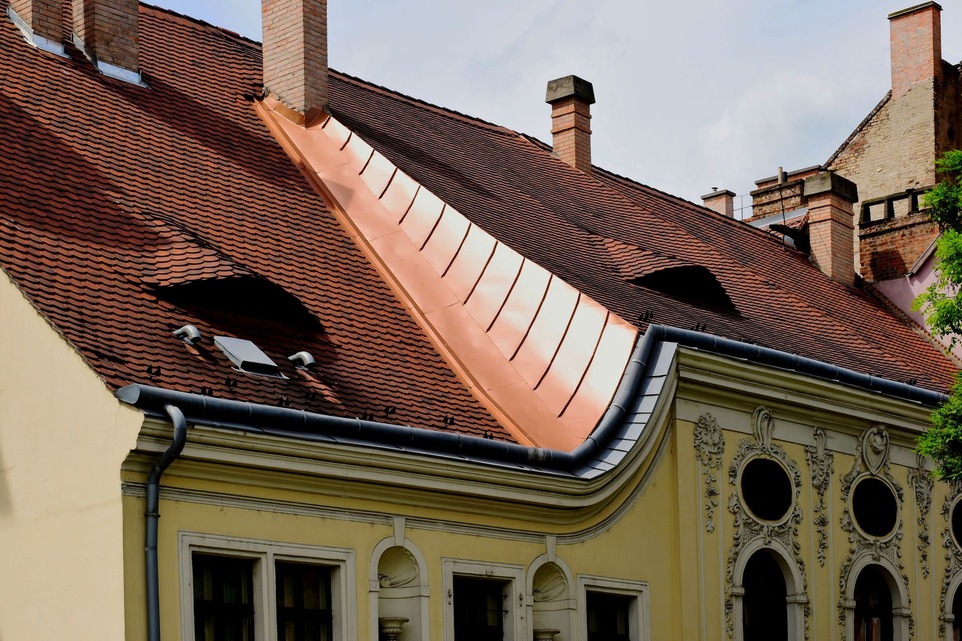Red-tiled roof with a large copper seam and chimneys on a yellow building.
