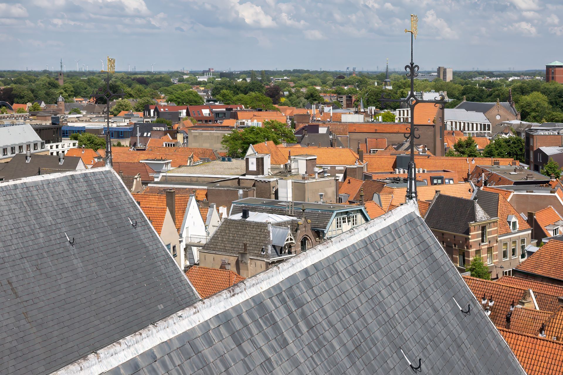 Aerial view of a town with red-tiled rooftops and a tall church spire under a cloudy sky