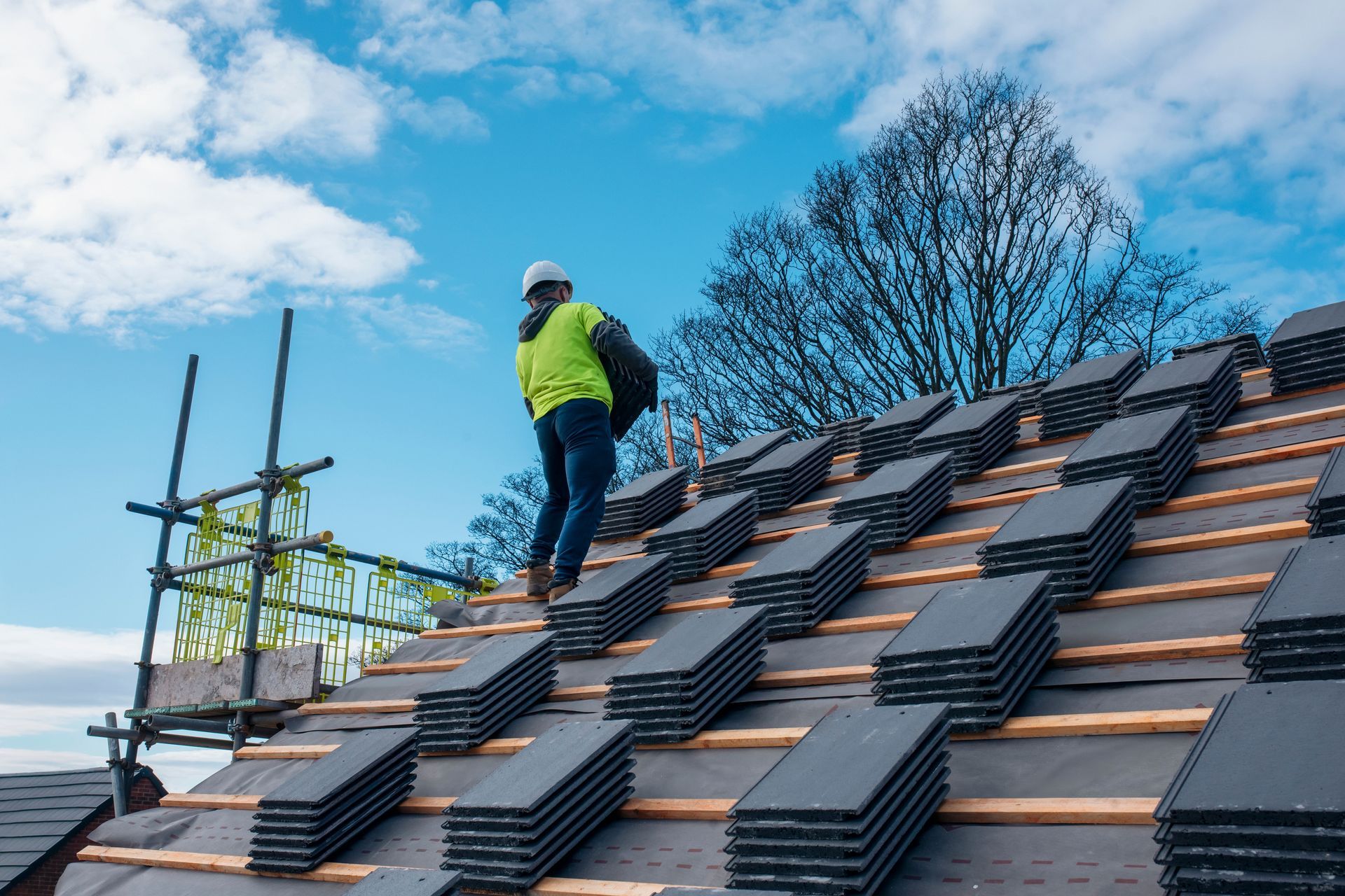 Worker installing roof tiles on a steep roof under a blue sky