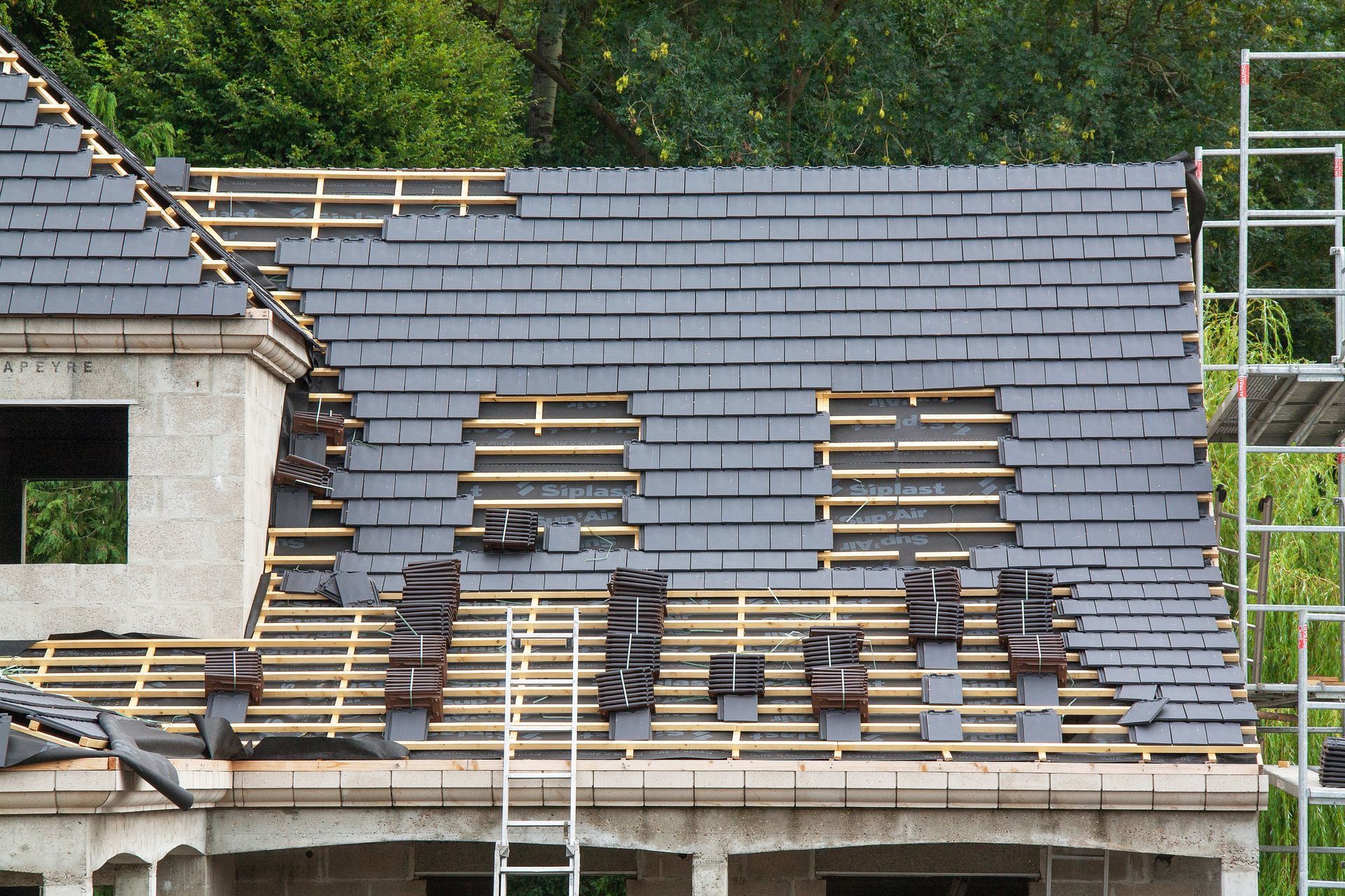 Partially roofed house under construction with exposed wooden rafters and gray shingles