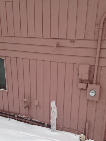 Snow-covered exterior wall with a utility meter, conduit, and a small window.