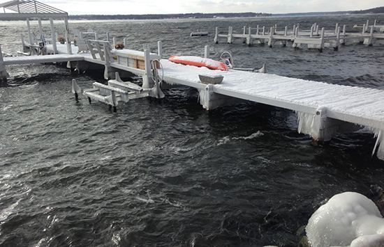 Snow-covered dock with a red-and-white boat tied up beside dark, choppy water