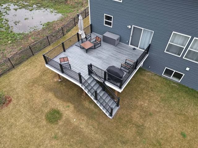 Covered wooden porch with railing, ceiling fan, and view of a grassy yard and homes beyond.