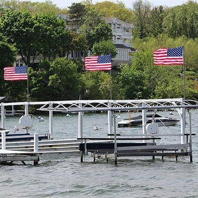 Dock on a lake with three American flags, trees, and houses in the background