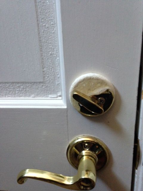 White door with brass deadbolt and curved handle, showing a worn lock plate near the edge.