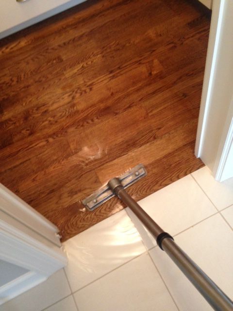 Steam mop cleaning a hardwood floor at the edge of a tiled doorway