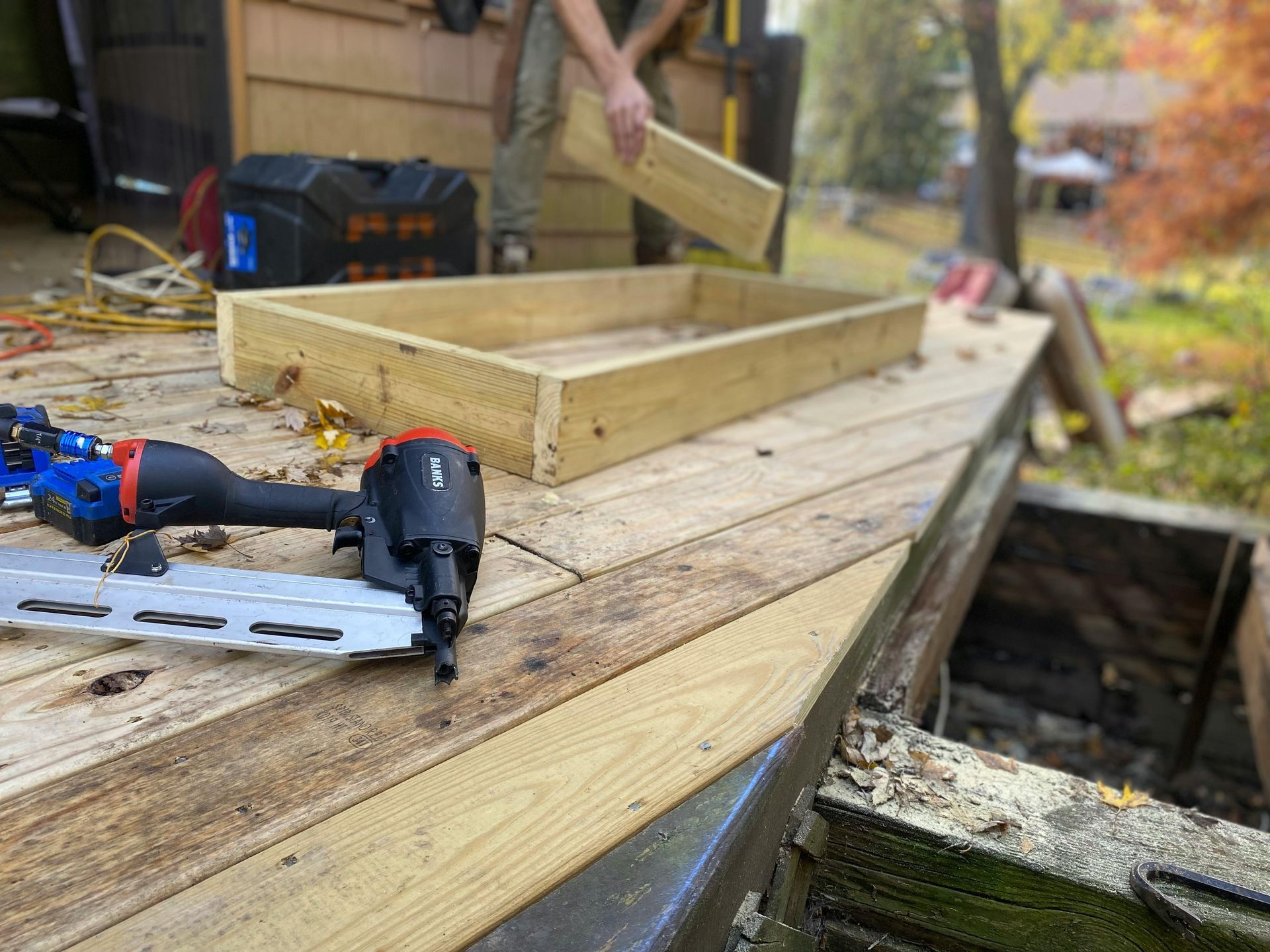 Drill and saw on a wooden workbench with a person building a wood frame outdoors