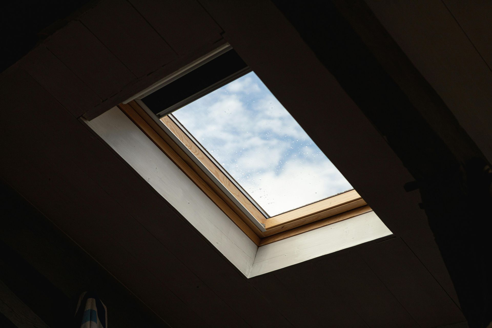 Open skylight with blue sky and clouds, set in a dark slanted ceiling.