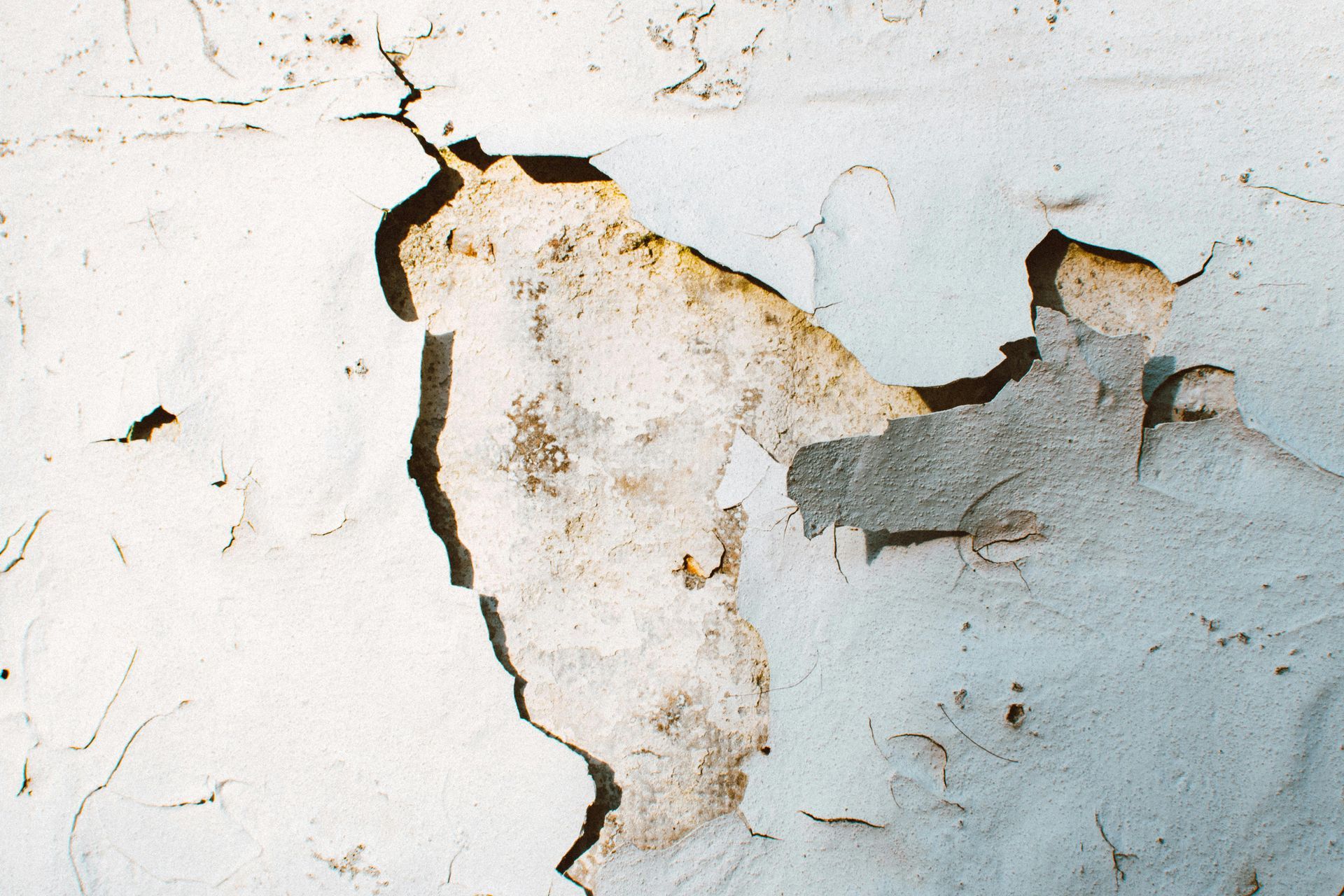 Cracked, peeling white wall with exposed brown plaster and chipped paint