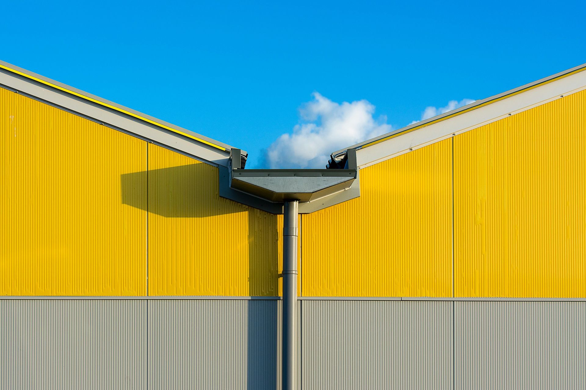 Yellow industrial building facades meeting at a central rooftop corner against a blue sky