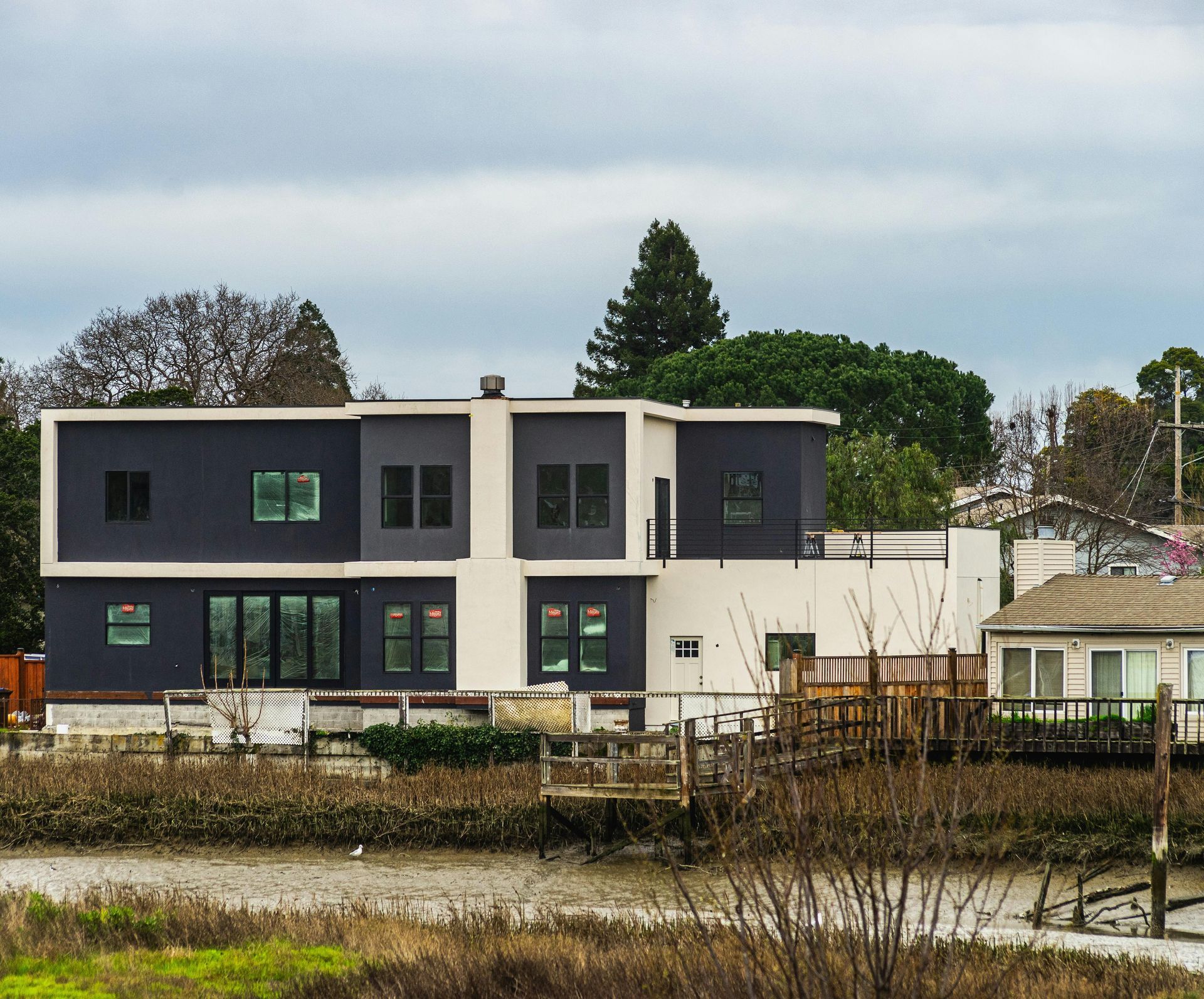 Modern two-story house with dark and white exterior beside a pond under an overcast sky
