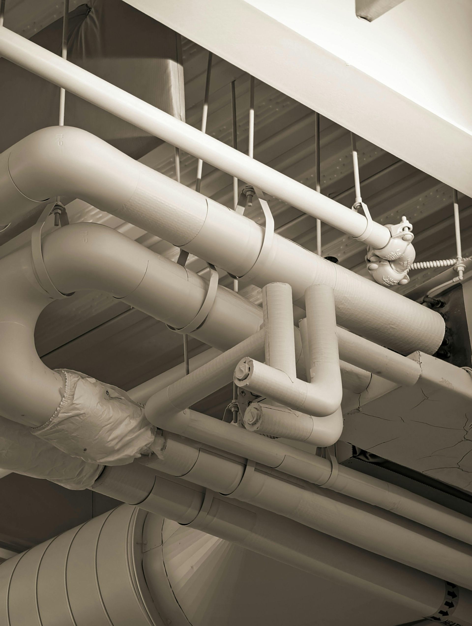 White industrial pipes and ducts running across a ceiling in an indoor utility space