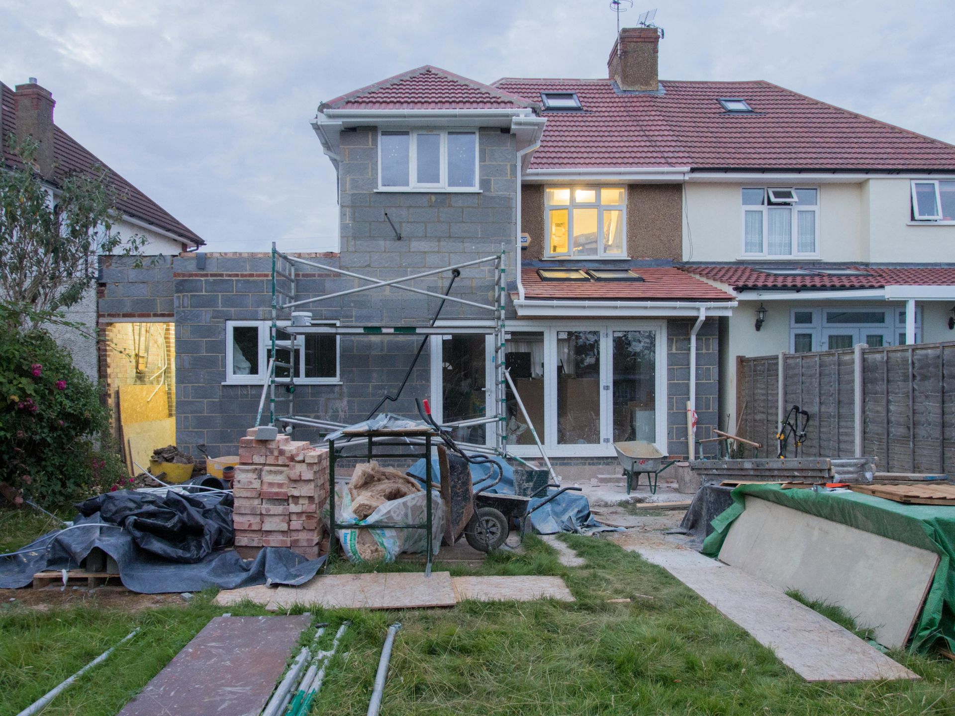 Backyard with a two-story house, patio scaffolding, and building materials during renovation.