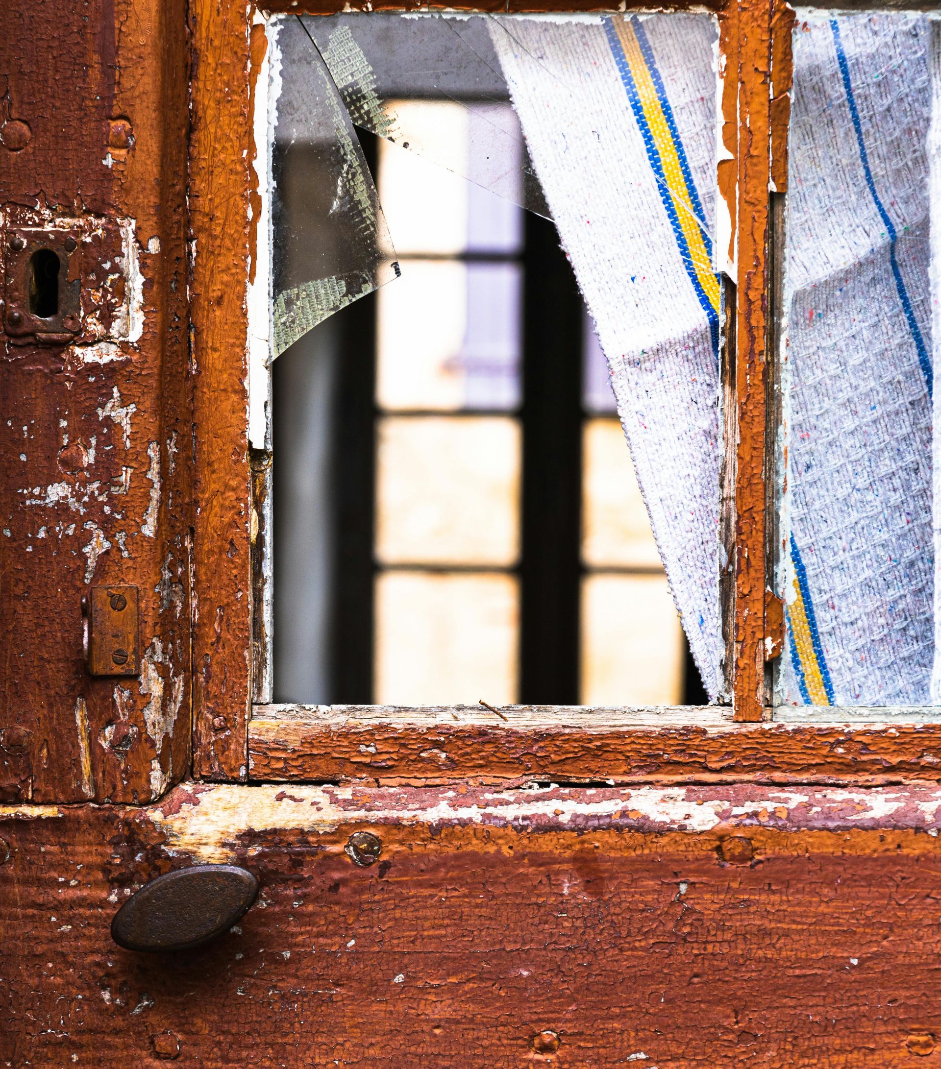 Close-up of a weathered wooden window with cracked glass and peeling paint, reflecting light.