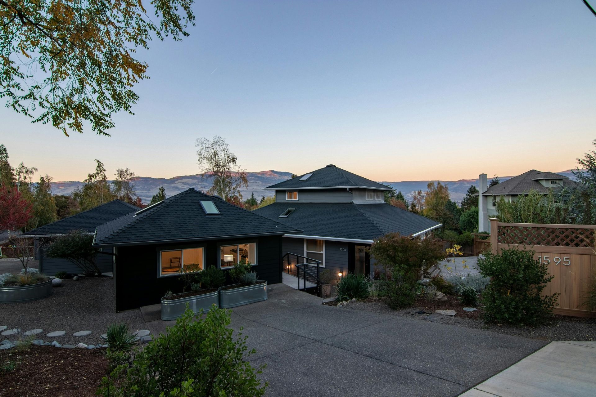 Suburban house at dusk with driveway, trees, and a view of rooftops and distant sky