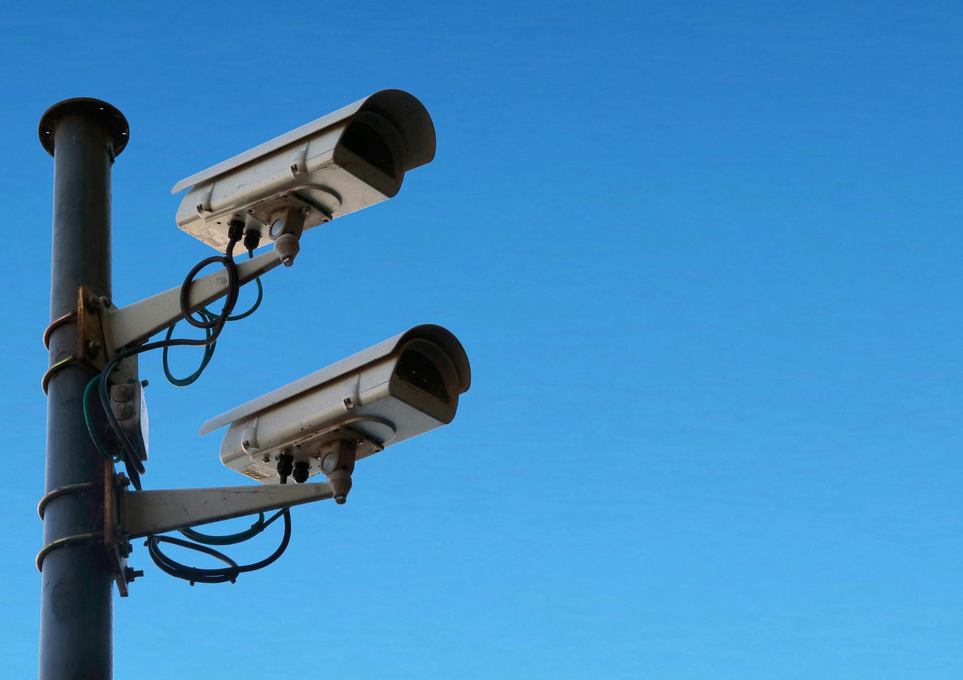 Two surveillance cameras mounted on a pole against a clear blue sky
