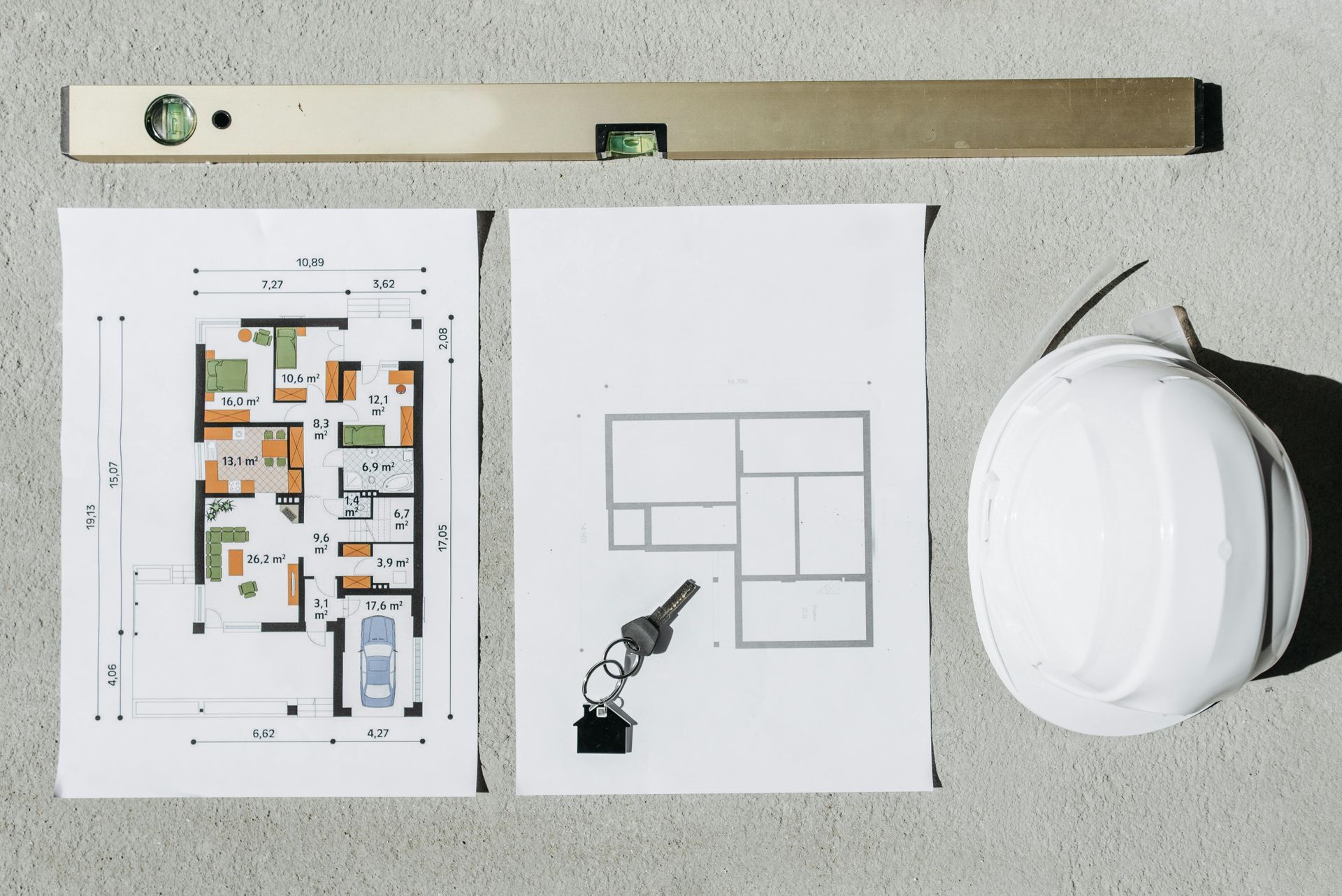 Floor plan drawings, pencil, and a white hard hat on a desk with a level above.