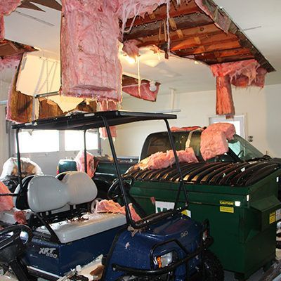 Golf cart in a garage under a ceiling with exposed pink insulation hanging down and debris scattered around.