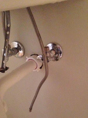Under-sink plumbing with hoses and chrome shutoff valves against a beige cabinet interior