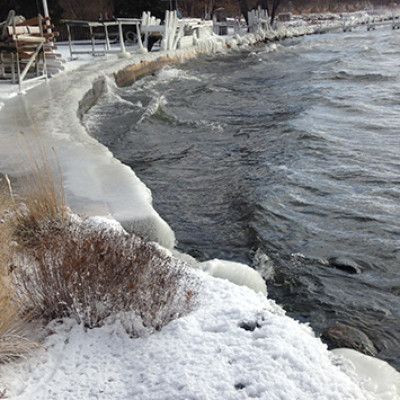 Snowy riverbank with icy water and a curved concrete embankment on a winter day