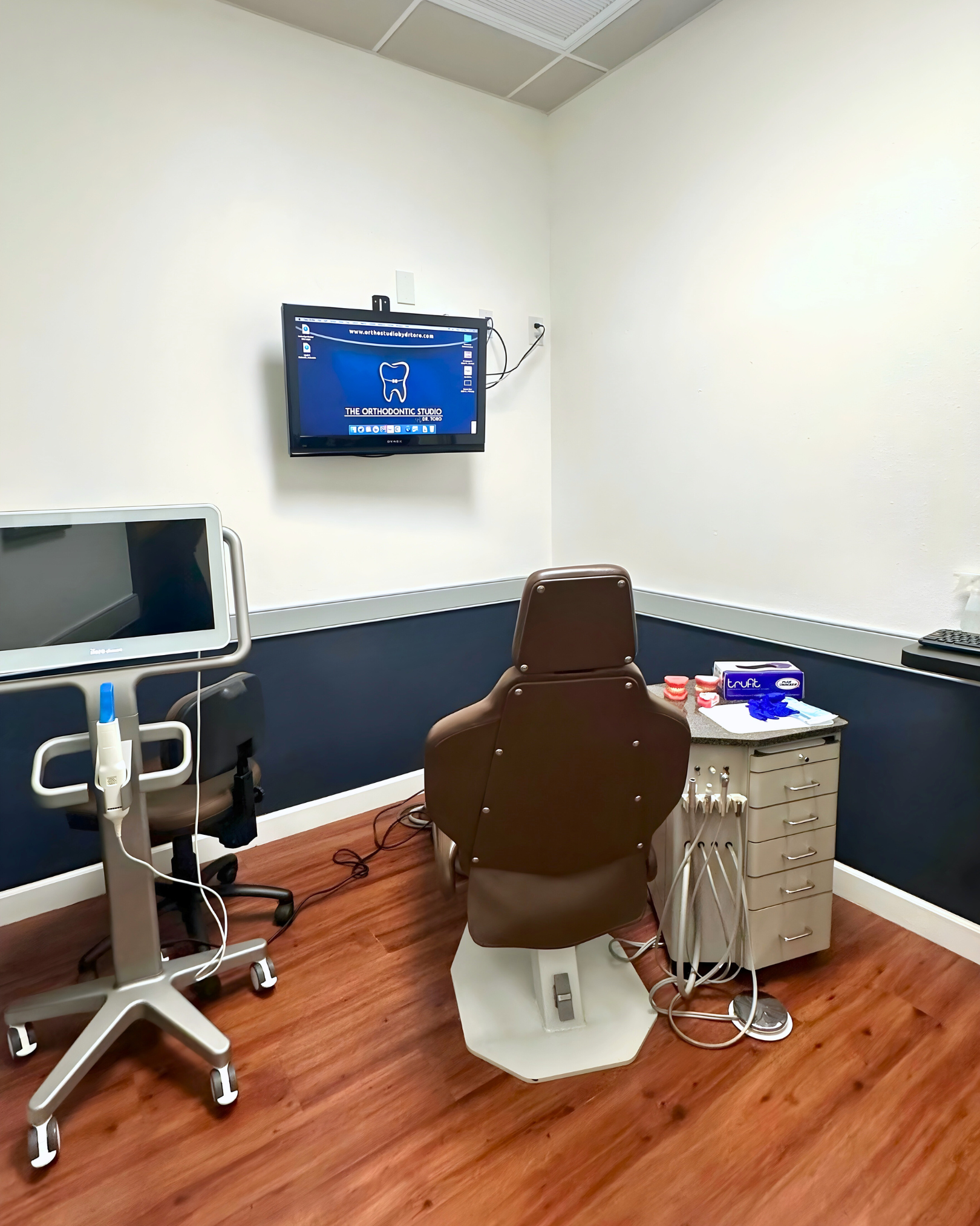 Dental exam room with chair, equipment, monitor, and blue and white walls.
