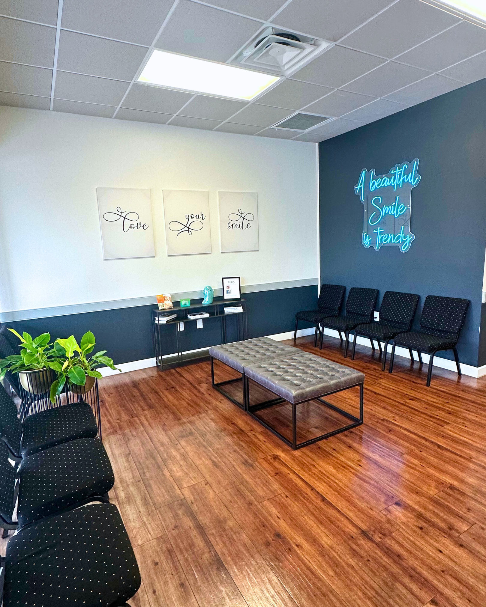 Waiting room with wooden floor, black chairs, gray bench, and teal accent wall with neon sign.