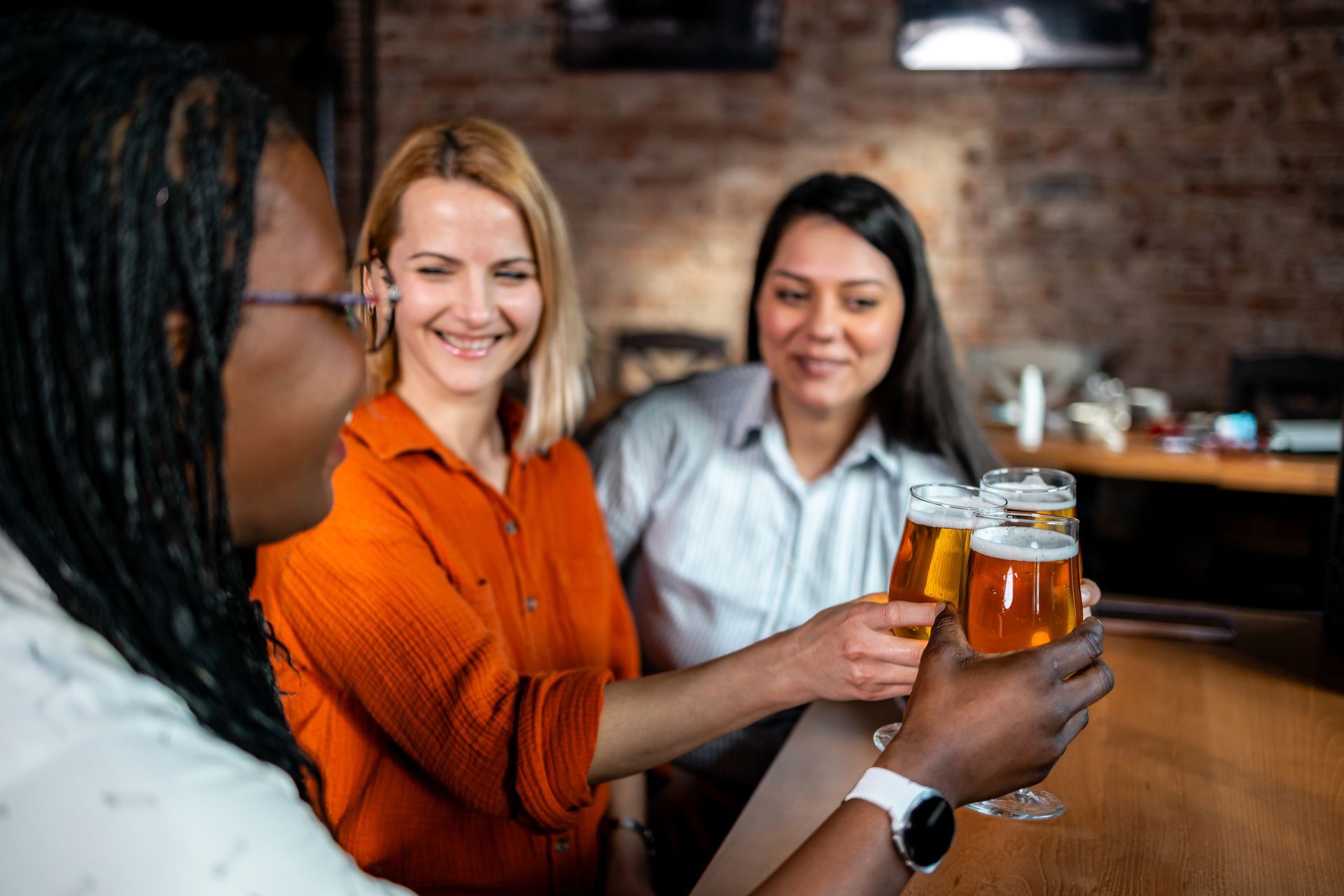 Three people cheers with glasses of beer in a rustic bar setting.