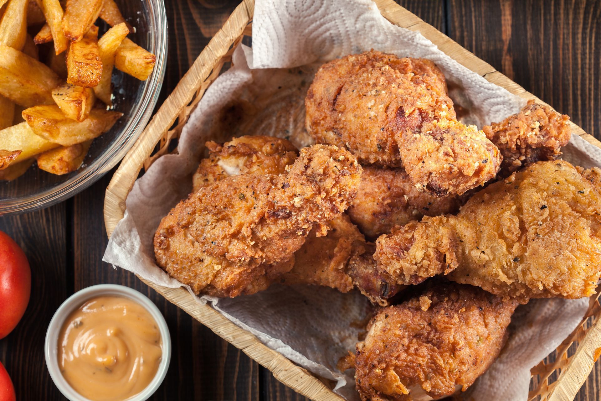 A basket filled with golden-brown fried chicken, served with a side of fries and a small bowl of dipping sauce.