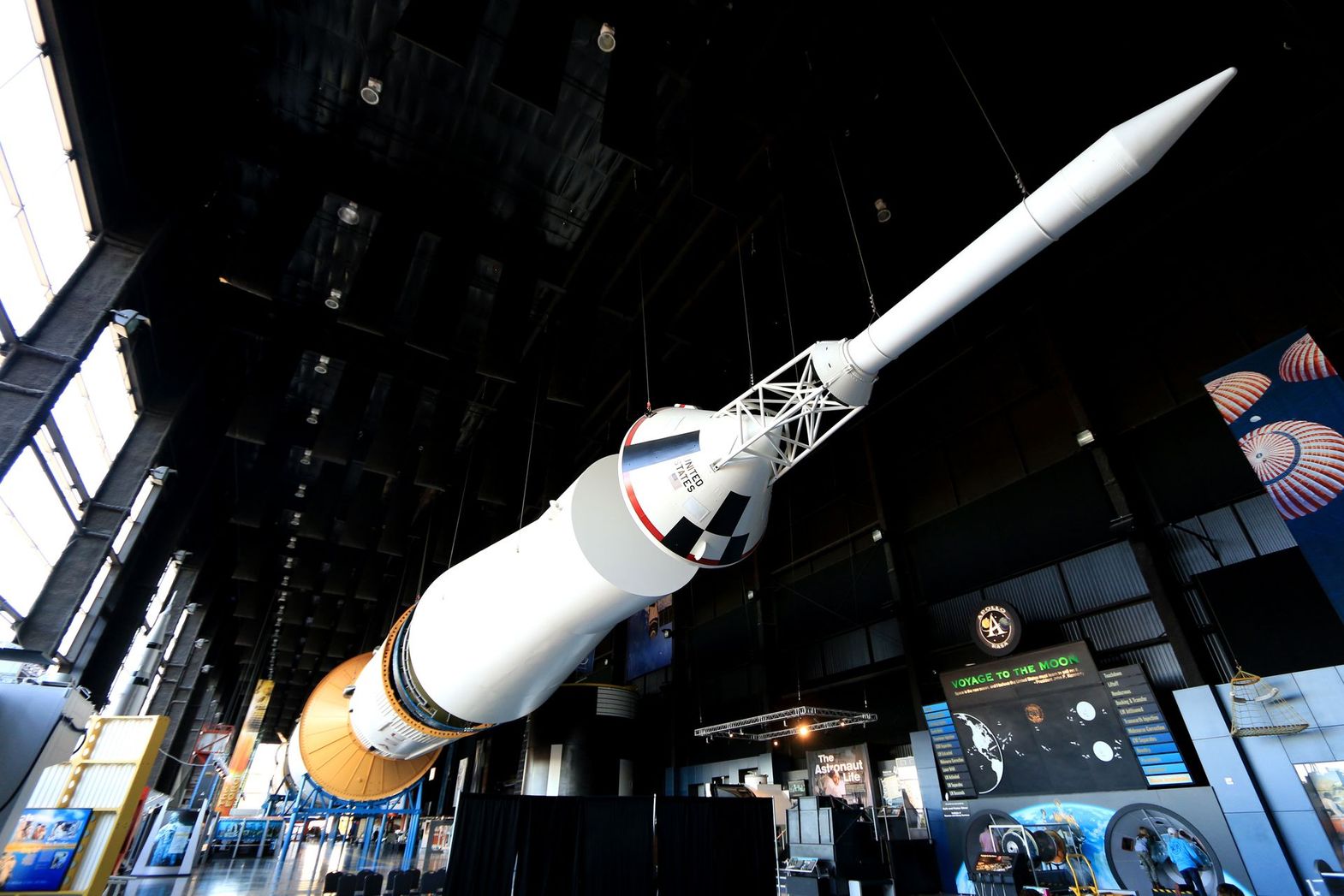 A large Saturn V rocket suspended horizontally inside a dark, industrial museum display hall.