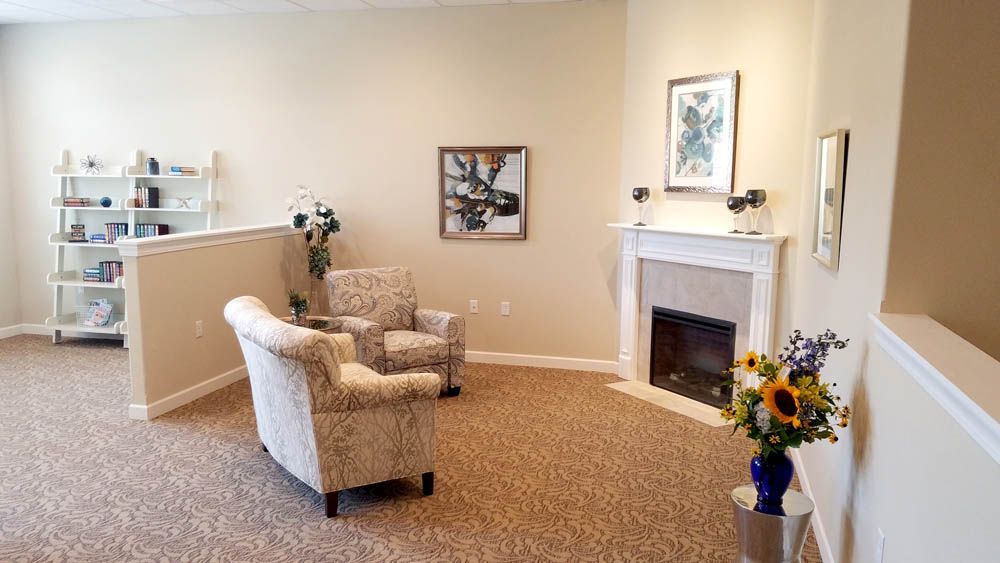 A living room with a fireplace , chairs , and a vase of flowers.