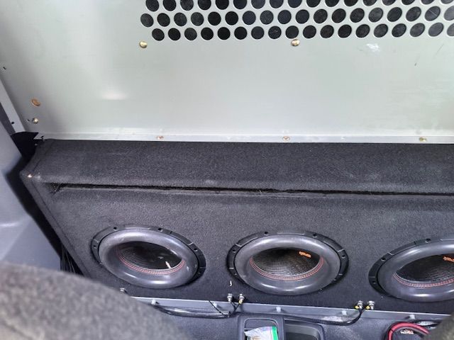 Three car subwoofers in a black box, with a metal grill above. Three car subwoofers in a black box, with a metal grill above.