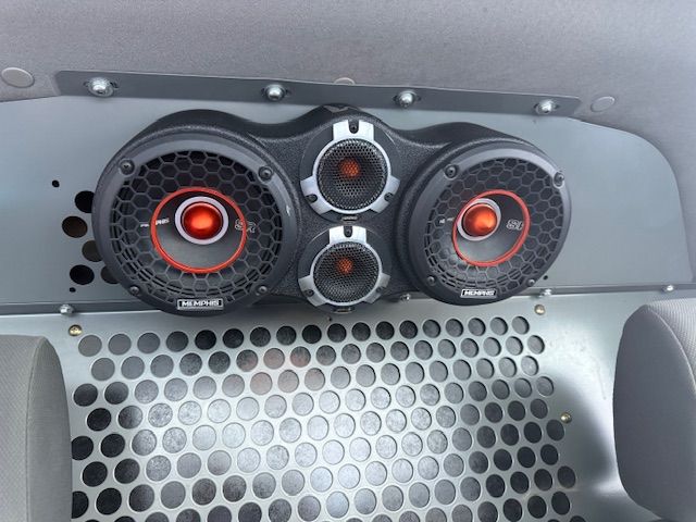 Three car speakers mounted on a metal panel; black and red accents, central to a vehicle. Three car speakers mounted on a metal panel; black and red accents, central to a vehicle.