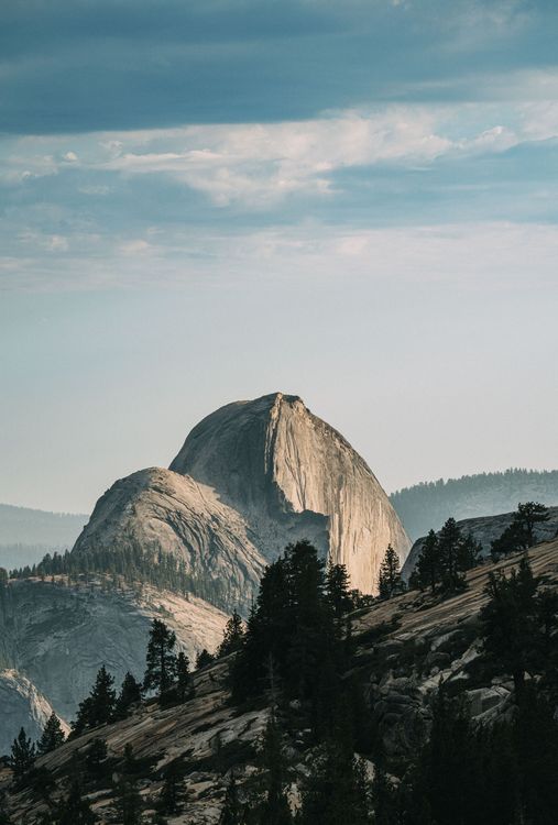 Rocky mountain peak at dawn with dark pine-covered slopes under a pale blue sky