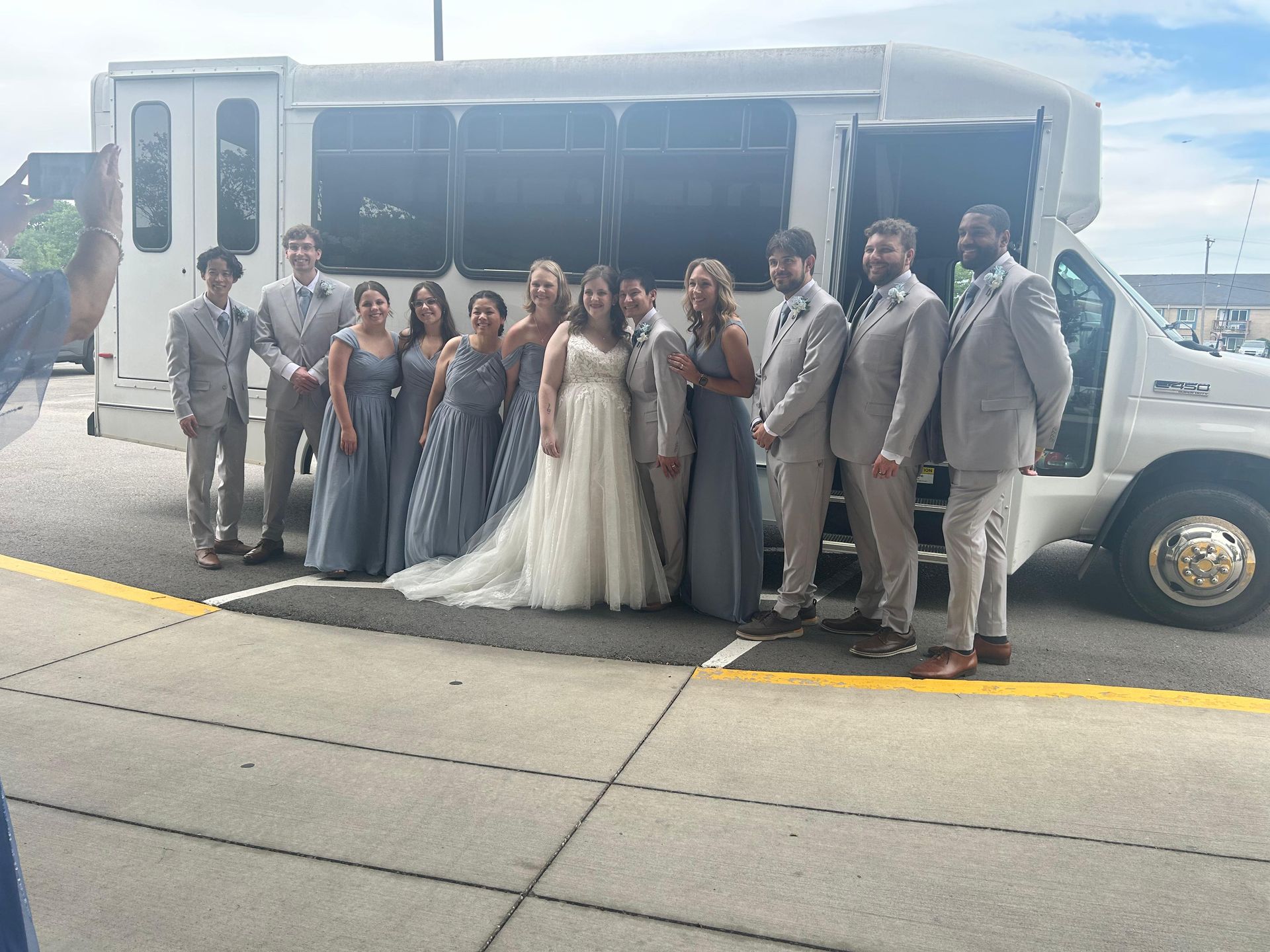 Wedding party posing beside a white shuttle bus on a city street