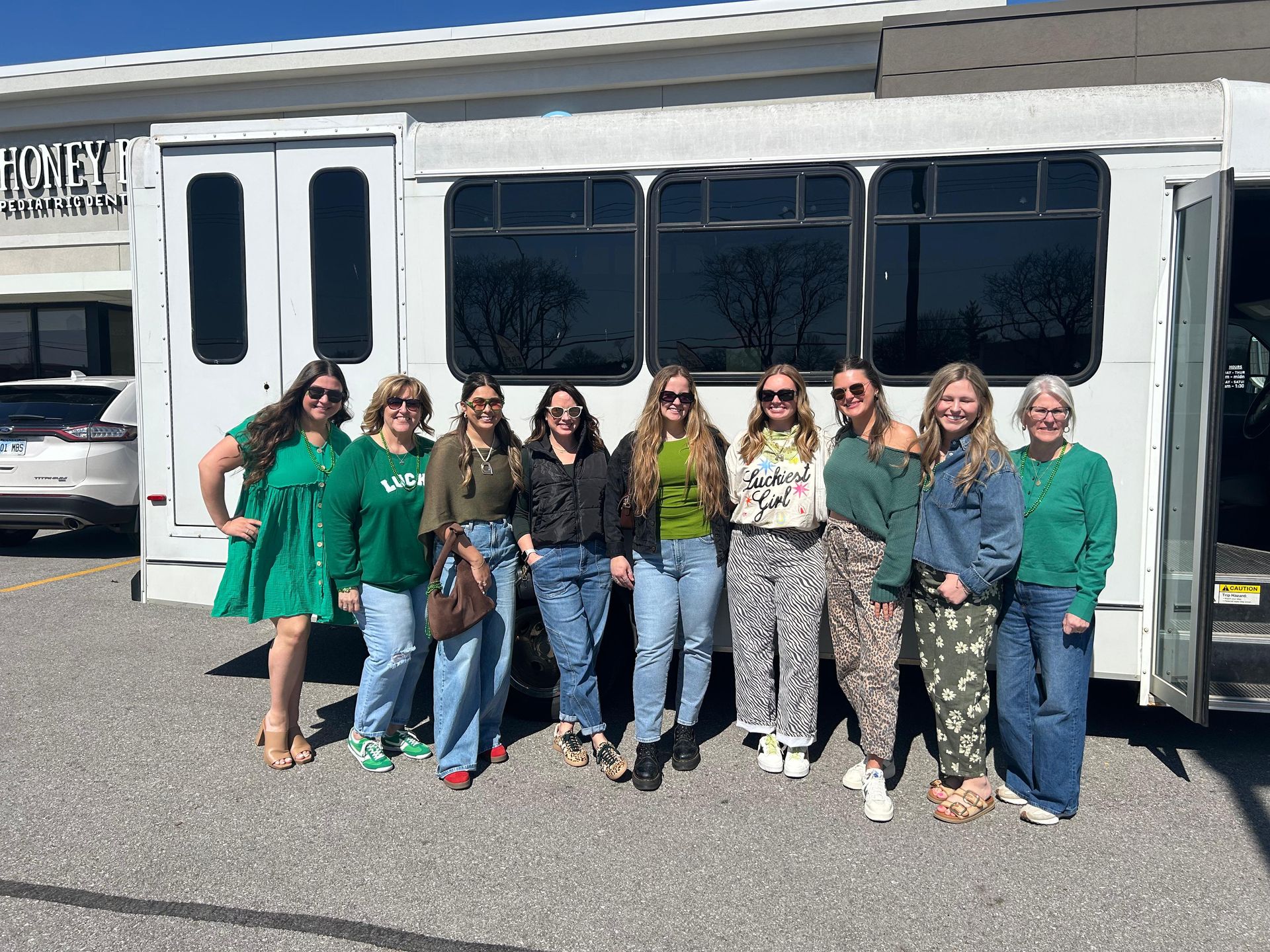 Group of smiling people standing in front of a white shuttle bus in a parking lot