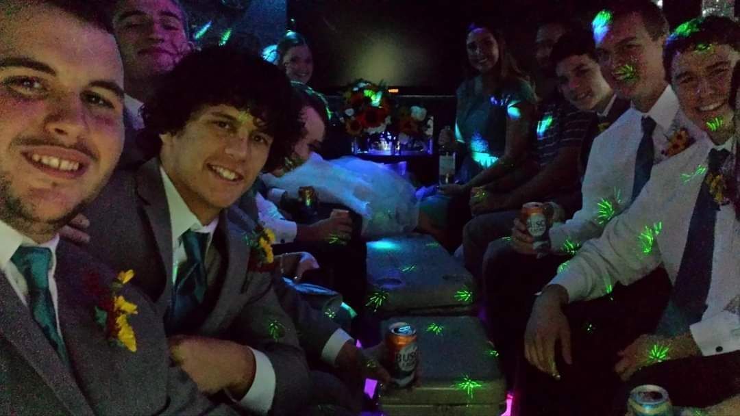 Group of people in formal wear seated at a dimly lit party table, smiling with colorful lights around them