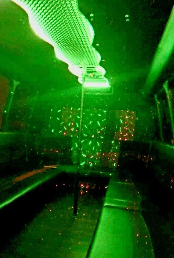 Green-lit interior of a bus or train with laser dots and a central pole.