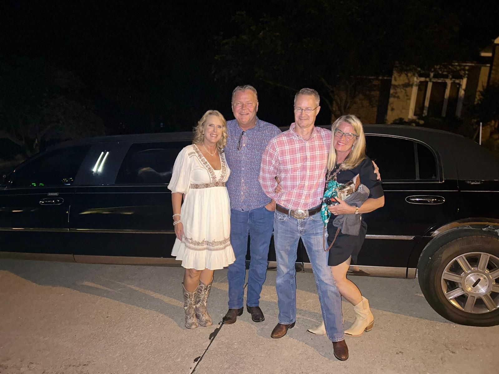 Four people posing in front of a black limousine at night.