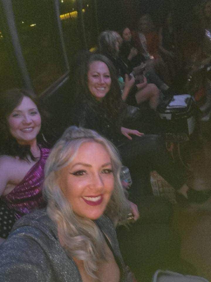 Smiling people seated together in a dimly lit venue, one holding a drink.