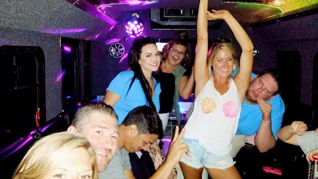 Group of friends dancing and smiling inside a neon-lit party bus