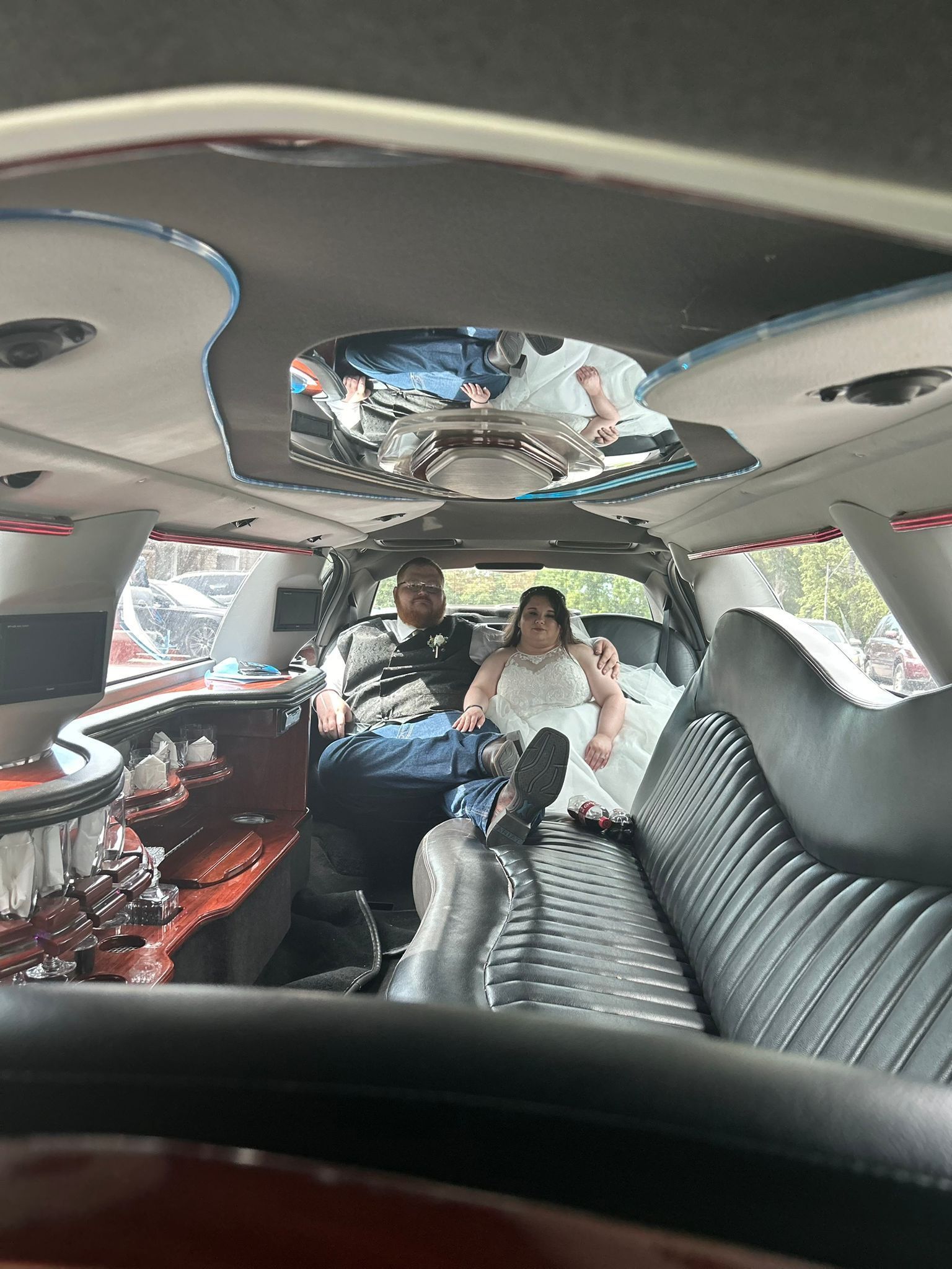 Two people sitting in a decorated limousine interior with mirrored ceiling and black quilted seats