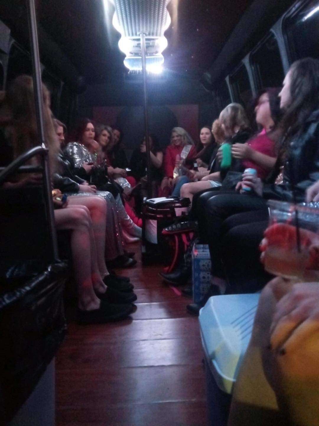 People sitting in a dim party bus, chatting under bright overhead lights, with drinks on the floor and seats.