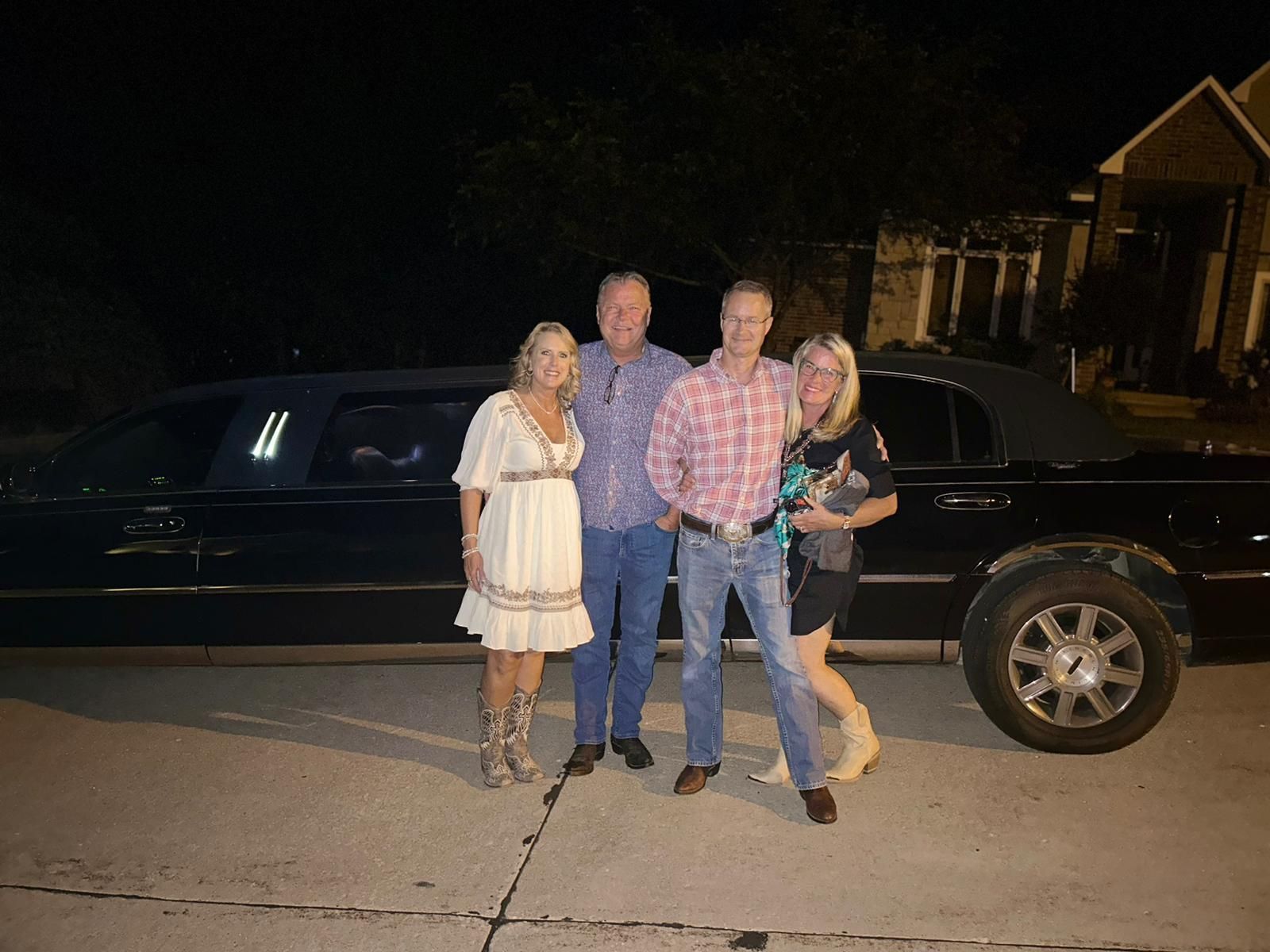 Four people standing in front of a black car at night on a residential street.