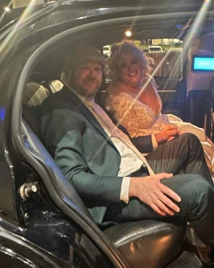 Two people seated in a luxury car, smiling at the camera in a dimly lit interior