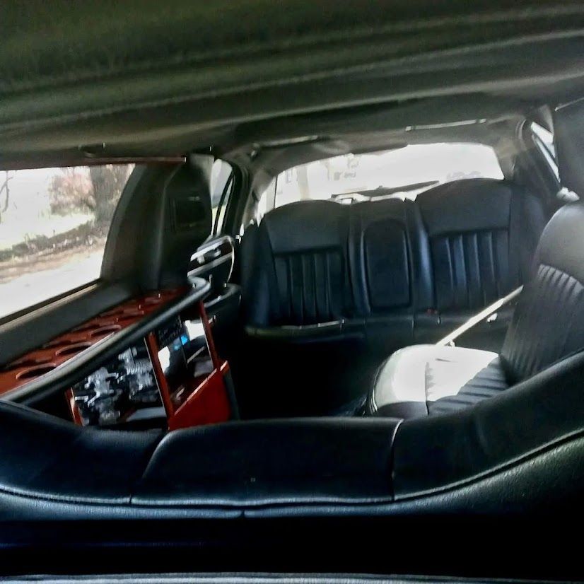 Interior of a vintage car with black leather seats and wood-trimmed dashboard, viewed from the rear.