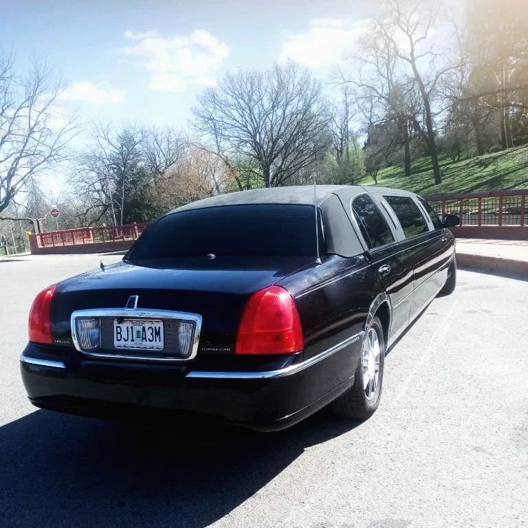 Black stretch limousine parked on a road beside a red bridge and bare trees on a sunny day