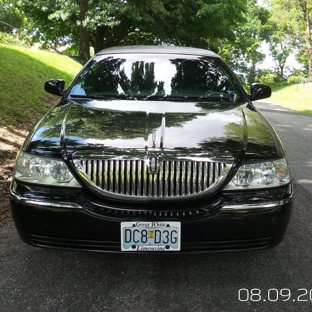 Black sedan parked on a tree-lined road, front view with chrome grille.
